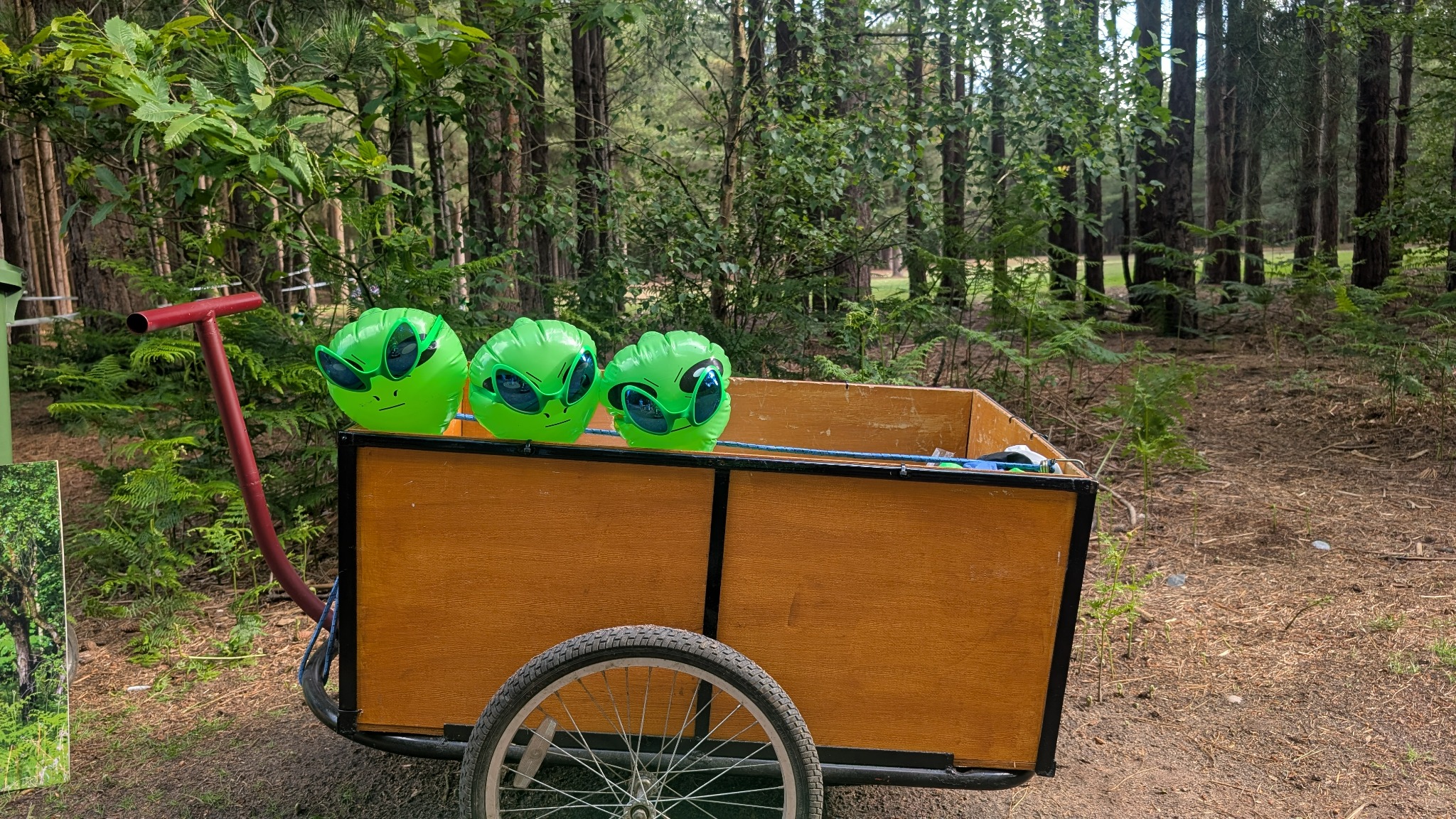 Three inflatable aliens peeking over the side of a trolley in Rendlesham Forest